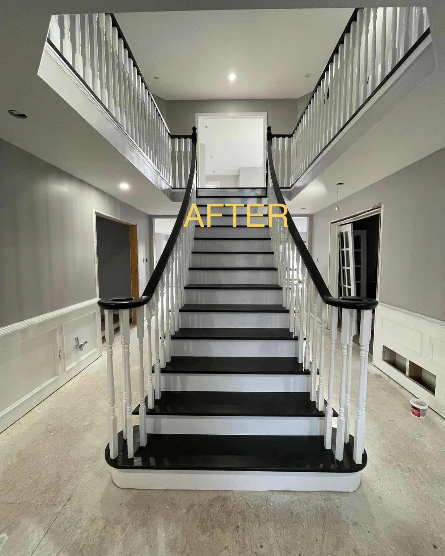 Grand two-story staircase after transformation with gloss black treads and crisp white spindles