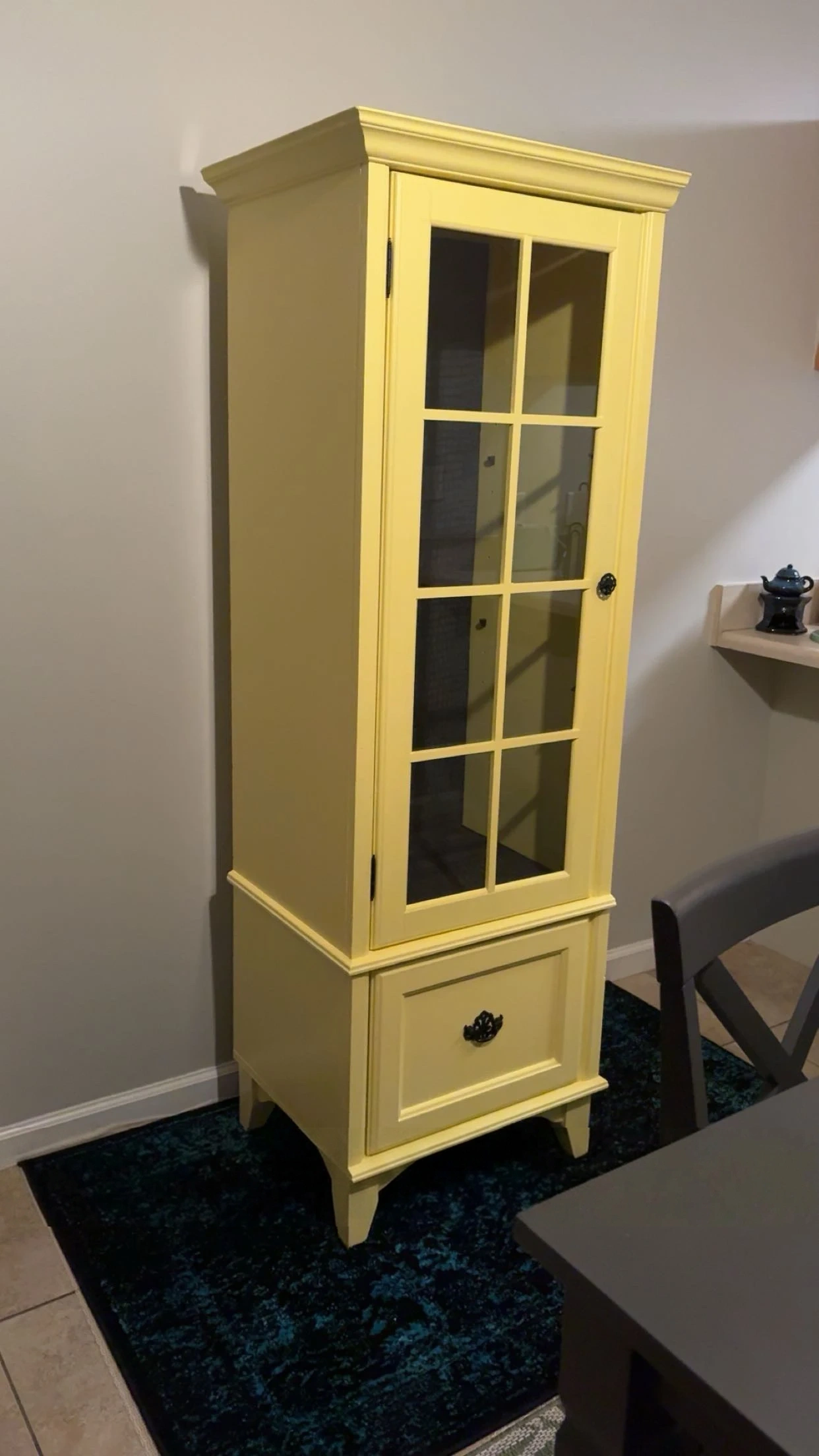 Vintage curio cabinet refinished in bright cheerful yellow with ornate black hardware