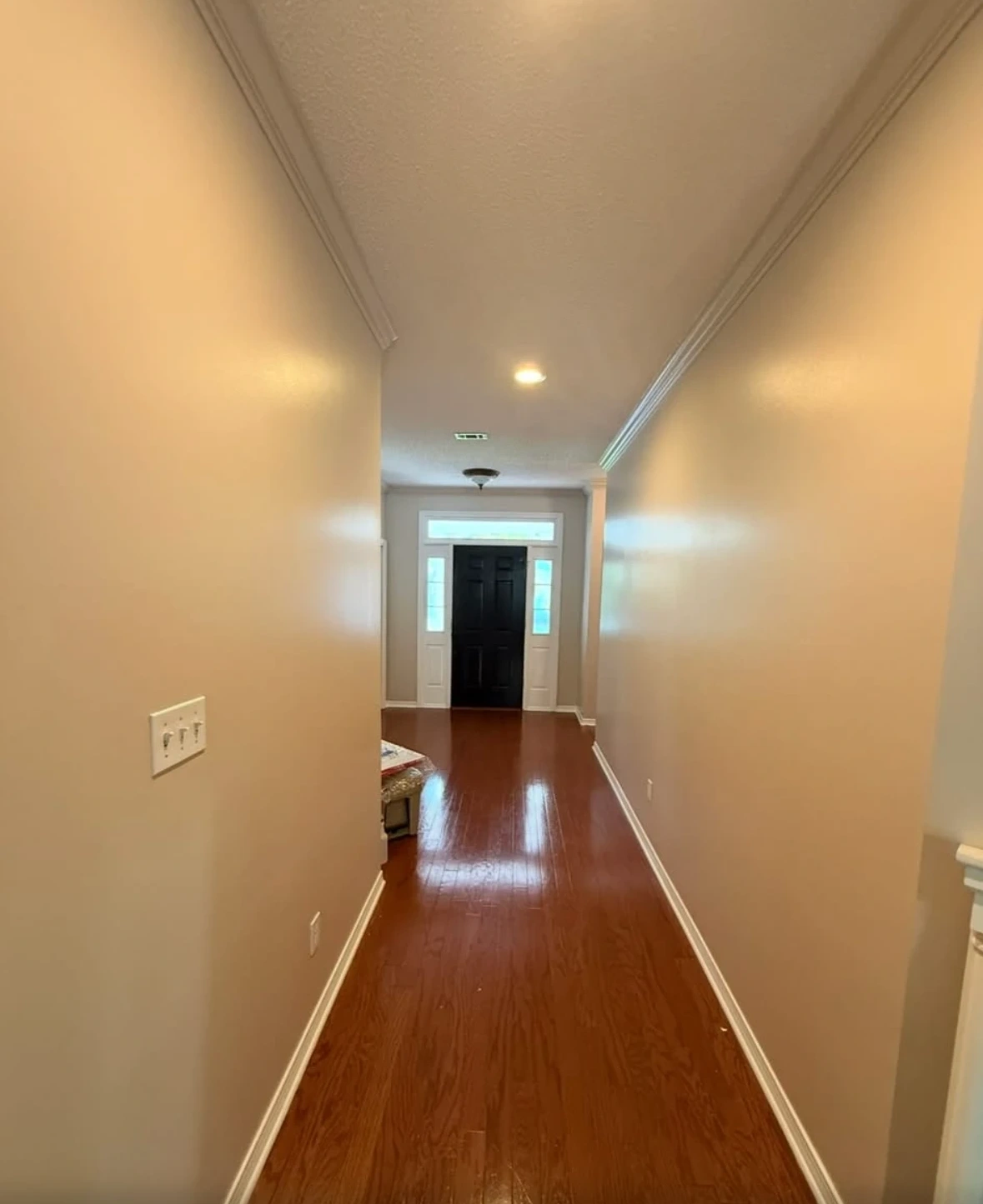 Long elegant hallway with hardwood floors, greige walls, and black front door