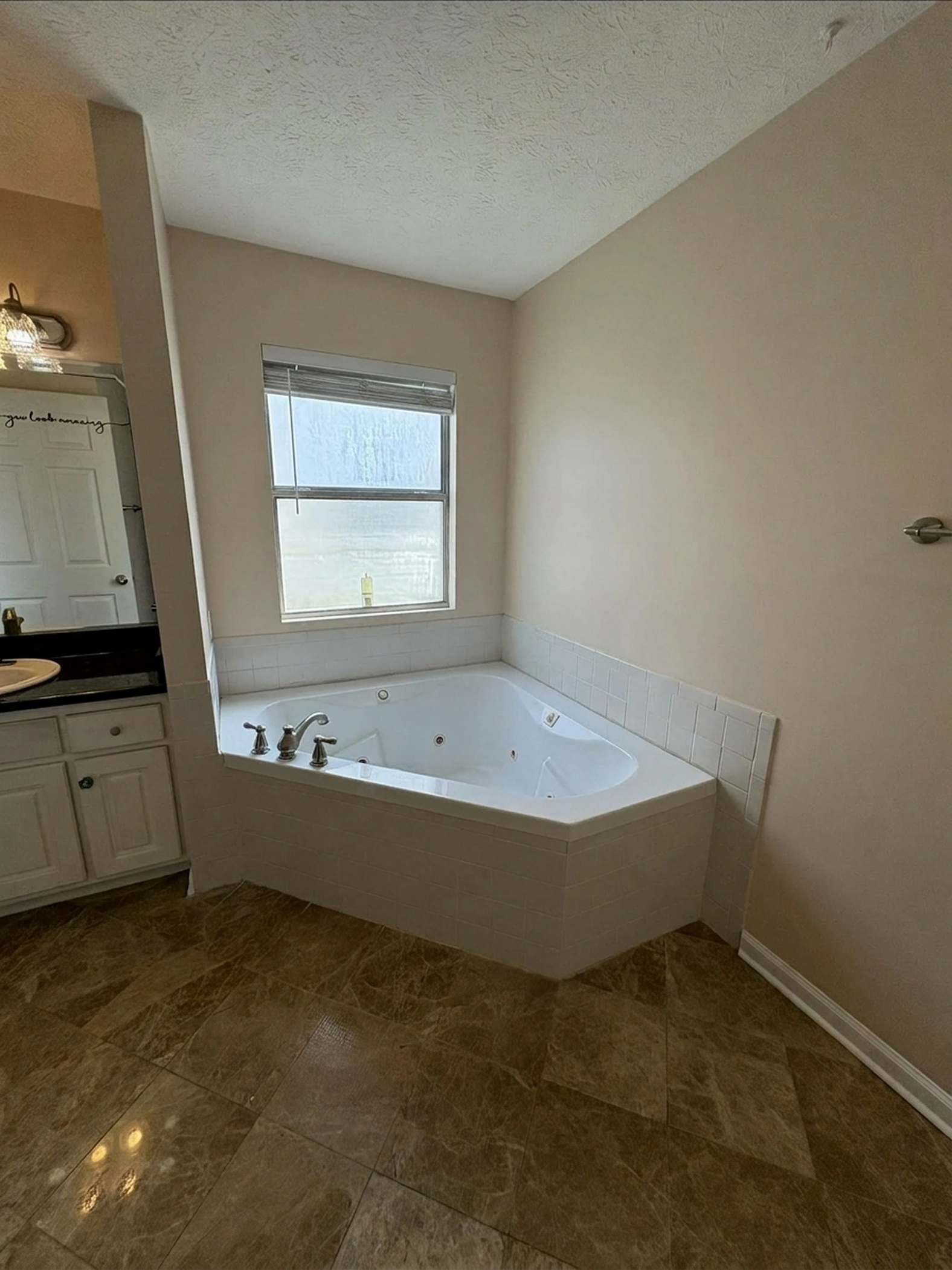 Master bathroom retreat featuring corner jacuzzi tub, white vanity, and warm beige walls